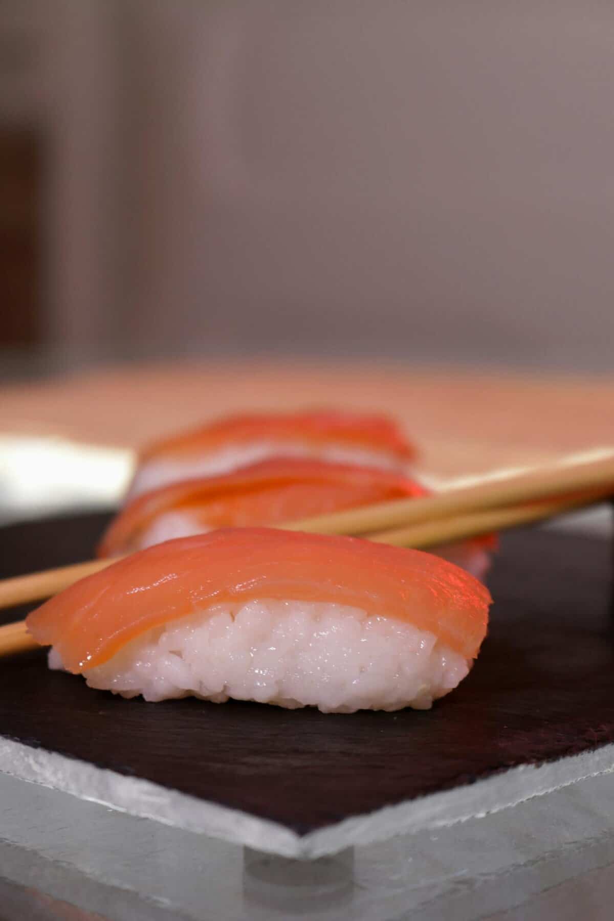 Delicious fresh salmon sushi nigiri served on slate with chopsticks in elegant presentation.