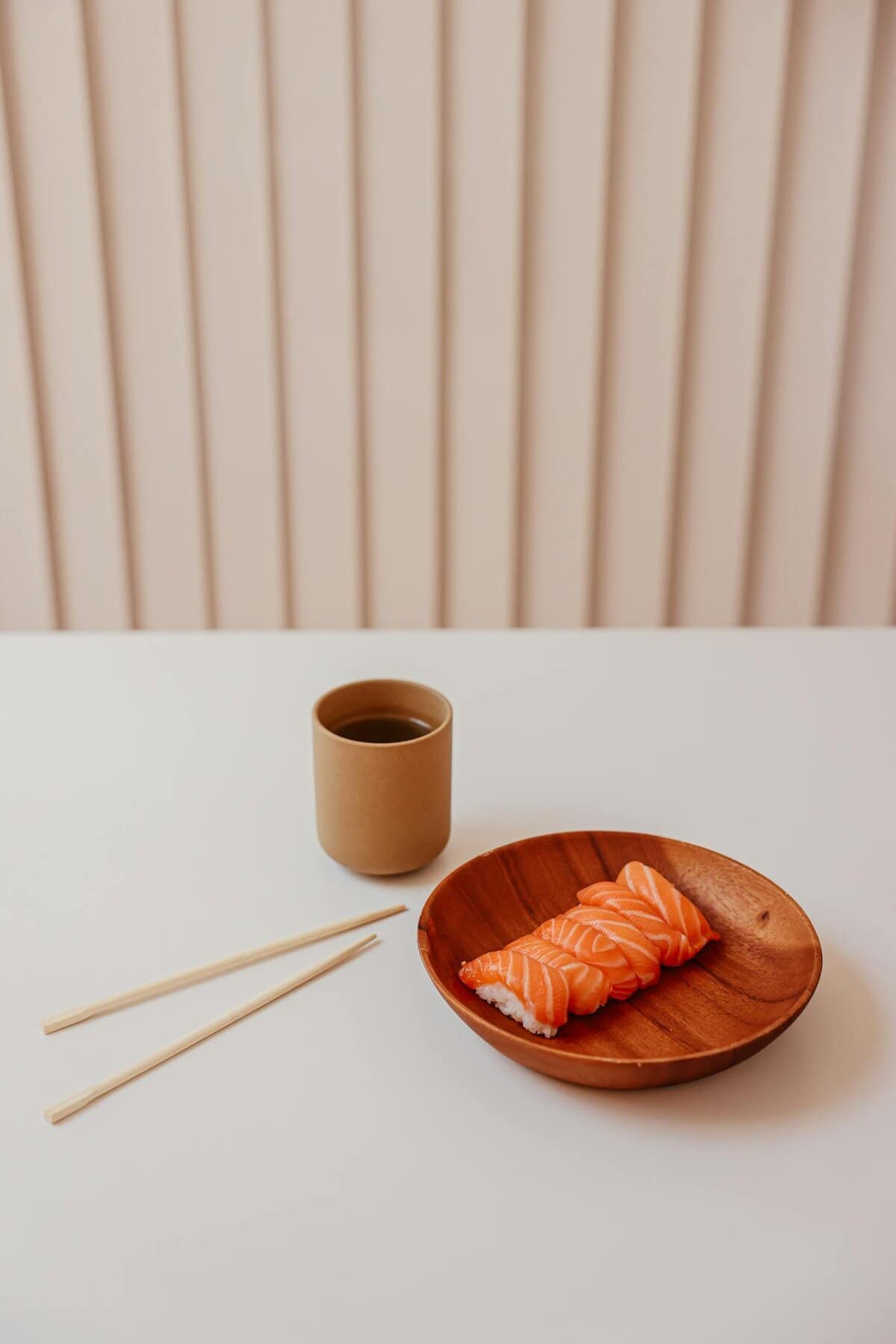 Minimalist display of salmon nigiri sushi and tea on a wooden plate, emphasizing Japanese cuisine.